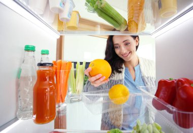 Sağlıklı yiyecek, sebze ve meyvelerle dolu açık buzdolabının yanında duran kadın portresi. Kadın portresi