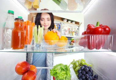Sağlıklı yiyecek, sebze ve meyvelerle dolu açık buzdolabının yanında duran kadın portresi. Kadın portresi