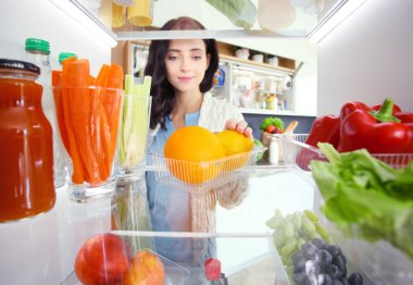 Sağlıklı yiyecek, sebze ve meyvelerle dolu açık buzdolabının yanında duran kadın portresi. Kadın portresi