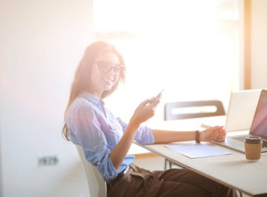 Ofis masasında oturan ve cep telefonuyla konuşan genç ve güzel bir iş kadını. İş kadını