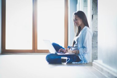 Dizüstü bilgisayar ile yerdeki genç güzel kadın evde oturuyor. Genç güzel kadın.