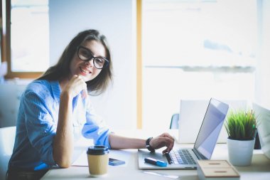 Ofis masasında oturan genç bir kadın dizüstü bilgisayar ekranına bakıyor. Genç kadın.