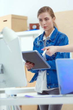 Masanın yanında duran iki genç kadın enstrüman, plan ve dizüstü bilgisayarla.