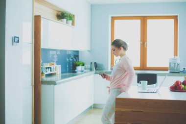 Cep telefonu ayakta modern mutfak kullanan kadın.