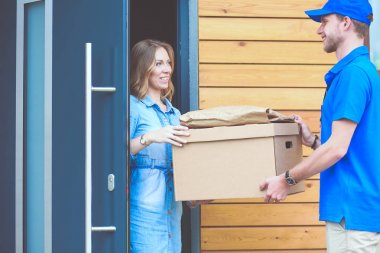 Mavi üniformalı gülümseyen kurye servis konseptine paket kutusu teslim eden teslimatçı. Mavi üniformalı gülümseyen teslimatçı.