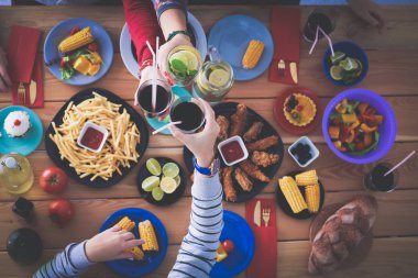 Ahşap masada otururken birlikte yemek yiyen bir grup insanın üst düzey görüntüsü. Masada yemek var. İnsanlar fast food yiyor..