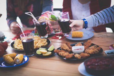 Ahşap masada otururken birlikte yemek yiyen bir grup insanın üst düzey görüntüsü. Masada yemek var. İnsanlar fast food yiyor..