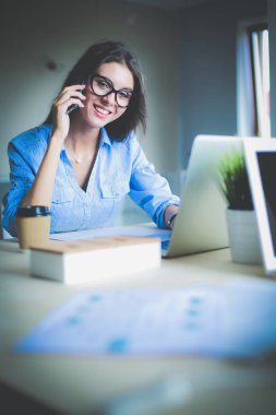 Ofis masasında oturan ve cep telefonuyla konuşan genç ve güzel bir iş kadını. İş kadını