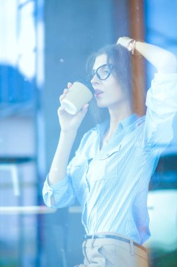 Ofis masasında dizüstü bilgisayarıyla oturan genç bir kadın. Pencereden bakıyor. Genç kadın.