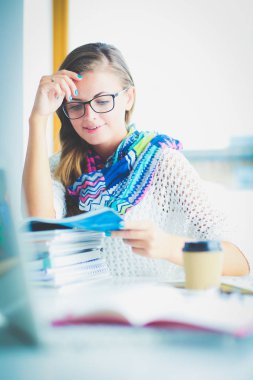 Kitapların arasında bir masada oturan genç bir kadın. Öğrenci