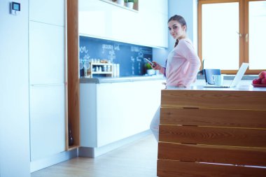 Cep telefonu ayakta modern mutfak kullanan kadın.