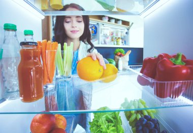 Sağlıklı yiyecek, sebze ve meyvelerle dolu açık buzdolabının yanında duran kadın portresi. Kadın portresi