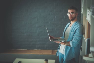 Duvarın yanında dizüstü bilgisayar tutan genç adam..