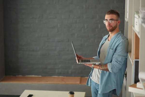 Young man holding laptop standing near wall. — Stock Photo, Image