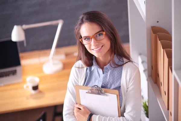 Giovane donna in piedi vicino alla scrivania con cartella del computer portatile e una tazza di caffè. Posto di lavoro. Donna d'affari. — Foto Stock
