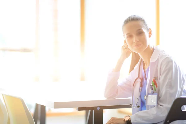 Hermosa joven y sonriente doctora sentada en el escritorio. Mujer doctora —  Fotos de Stock