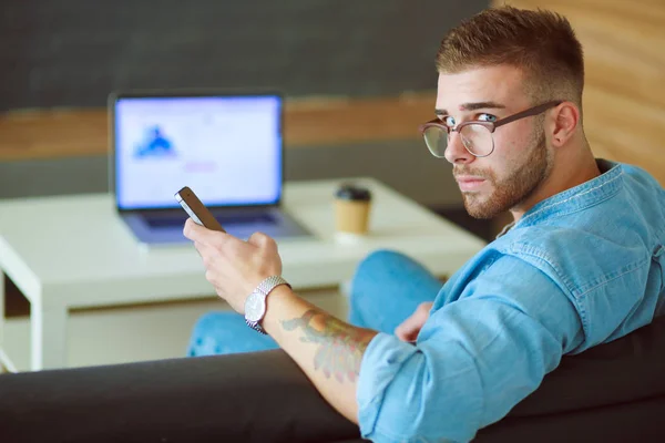 Jonge man met telefoon en werkt op de laptop. — Stockfoto