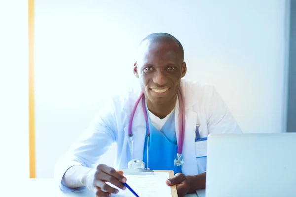 Portret van een jonge mannelijke arts die een headset draagt terwijl hij een computer gebruikt aan een bureau in de kliniek. Dokter.. — Stockfoto