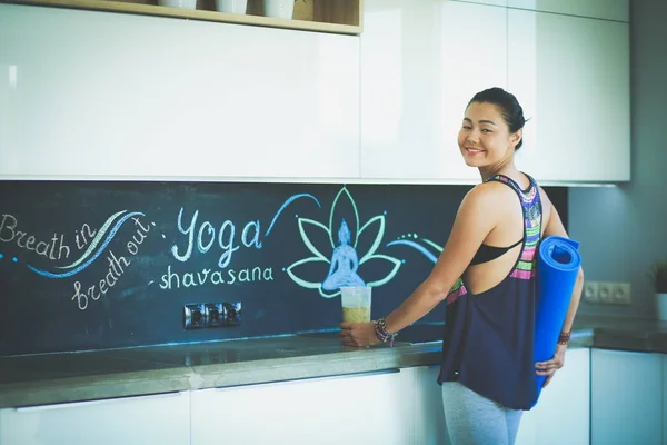 Retrato de una mujer sonriente sosteniendo en su mano una esterilla de yoga mientras estaba de pie en el estudio. Yoga. Una mujer. Bienestar — Foto de Stock