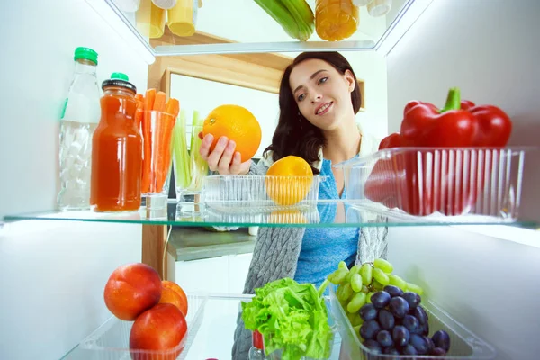 Портрет жінки, що стоїть біля відкритого холодильника, повний здорової їжі, овочів та фруктів. Портрет жінки — стокове фото