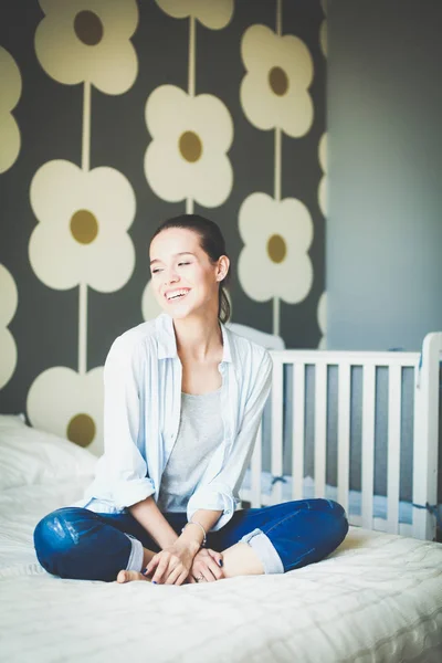 Mladá žena, sedící na posteli v dětské postýlce. Mladá maminka — Stock fotografie