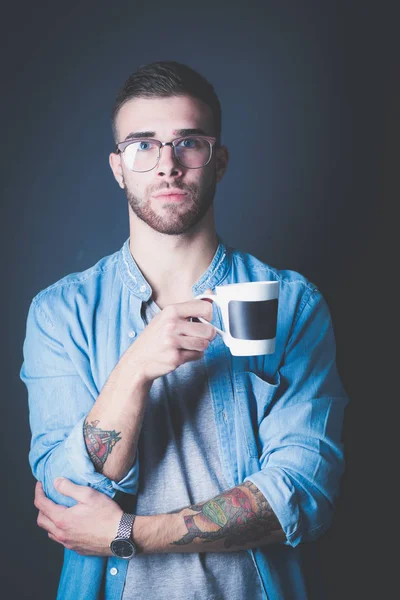 Retrato de un joven guapo de pie y sosteniendo una taza de café en sus manos — Foto de Stock