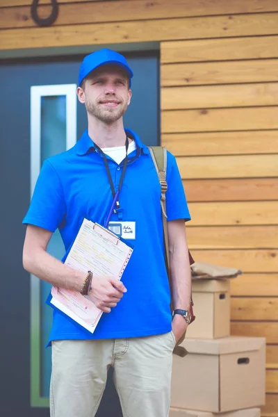 Repartidor sonriente con uniforme azul que entrega la caja de paquetes al destinatario: concepto de servicio de mensajería. Repartidor sonriente en uniforme azul — Foto de Stock