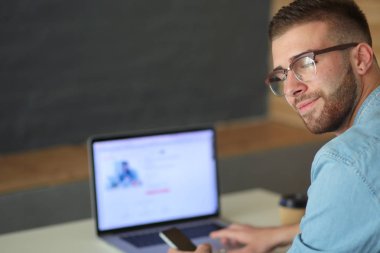 Genç adam kullanarak telefon ve dizüstü bilgisayarda çalışır.