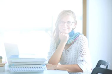 Kitapların arasında bir masada oturan genç bir kadın. Öğrenci