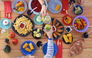 Ahşap masada otururken birlikte yemek yiyen bir grup insanın üst düzey görüntüsü. Masada yemek var. İnsanlar fast food yiyor..