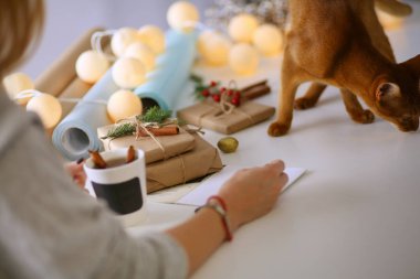 Noel hediye kutusu ile masaya oturan kadın. Kadının elleri