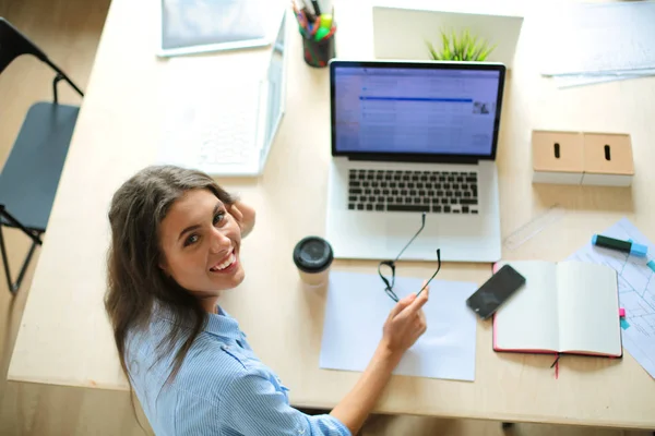 Egy fiatal nő ül az irodai asztalnál, a laptop képernyőjét bámulja. Fiatal nő — Stock Fotó