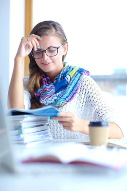 Kitapların arasında bir masada oturan genç bir kadın. Öğrenci