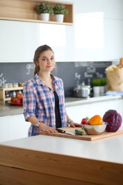 Masanın yanındaki mutfakta sebze doğrayan genç bir kadın..
