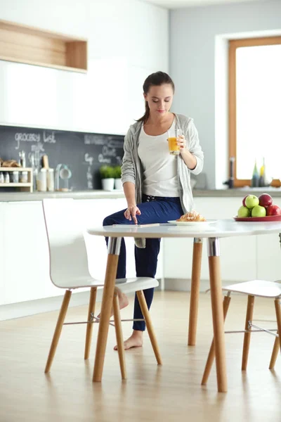 Mujer joven con jugo de naranja y tableta en la cocina. — Foto de Stock