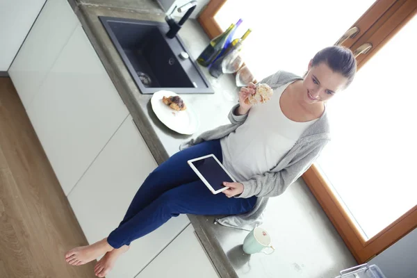 Hermosa joven usando una tableta digital en la cocina. — Foto de Stock