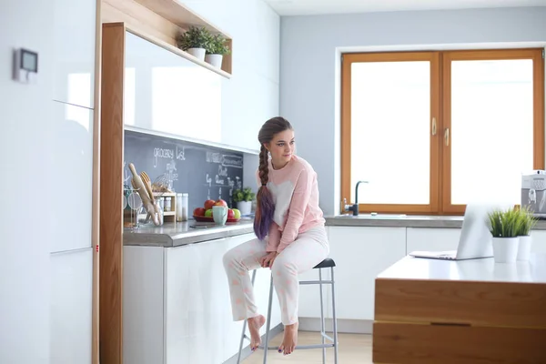 Jovem mulher sentada na mesa na cozinha . — Fotografia de Stock