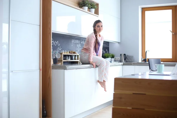 Jovem mulher sentada na mesa na cozinha . — Fotografia de Stock