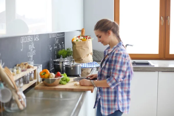 Mujer joven cortando verduras en la cocina cerca del escritorio . — Foto de Stock