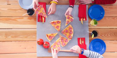 Ahşap masada otururken birlikte yemek yiyen bir grup insanın üst düzey görüntüsü. Masada yemek var. İnsanlar fast food yiyor..