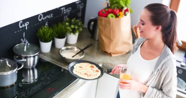 Genç bir kadın mutfakta krep pişiriyor sobanın yanında duruyor.