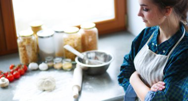 Mutfakta sobanın yanında duran genç bir kadın. .