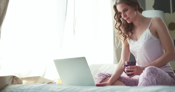 Ung vacker kvinna som sitter i sängen med laptop — Stockfoto