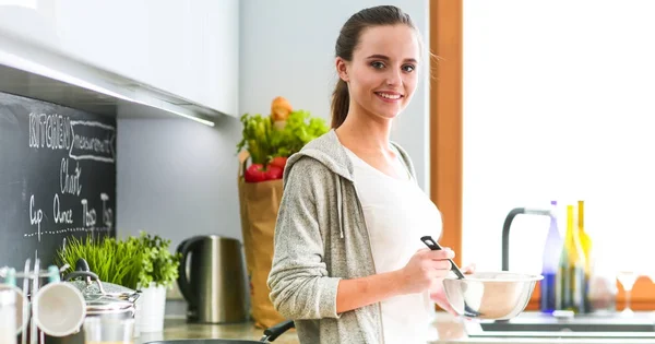 Jonge vrouw bereidt pannenkoeken in de keuken terwijl ze naast de tafel staat. Vrouw in de keuken. Koken in de keuken. — Stockfoto