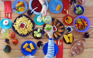 Ahşap masada otururken birlikte yemek yiyen bir grup insanın üst düzey görüntüsü. Masada yemek var. İnsanlar fast food yiyor..