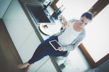 Mutfakta dijital tablet kullanan güzel genç bir kadın..