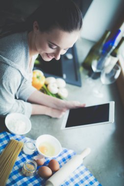 Güzel bir kadın mutfakta pasta pişiriyor. Masanın yanında duruyor..