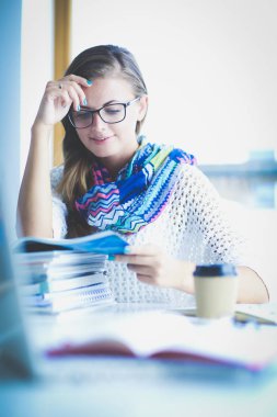 Kitapların arasında bir masada oturan genç bir kadın. Öğrenci