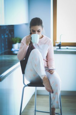 modern mutfakta otururken cep telefonu kullanan kadın.