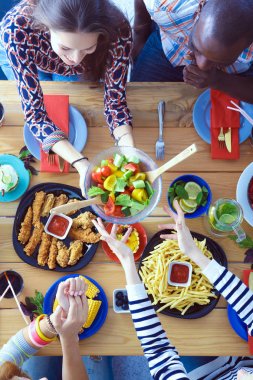 Ahşap masada otururken birlikte yemek yiyen bir grup insanın üst düzey görüntüsü. Masada yemek var. İnsanlar fast food yiyor..